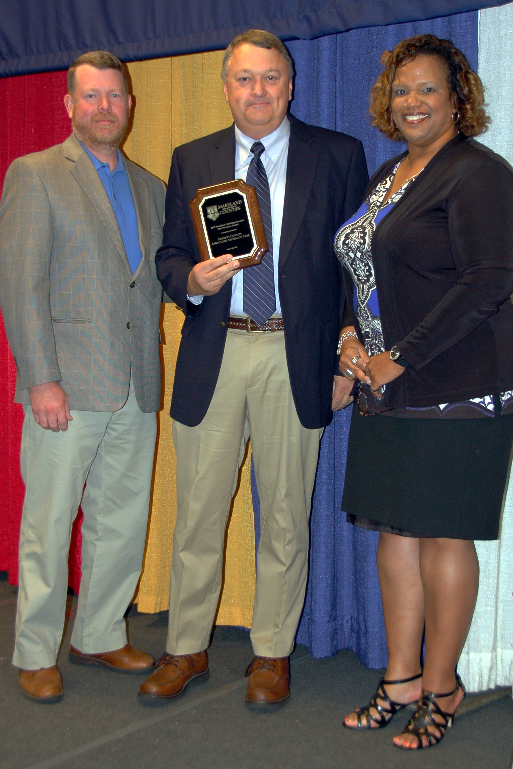 Man holding award next to two individuals